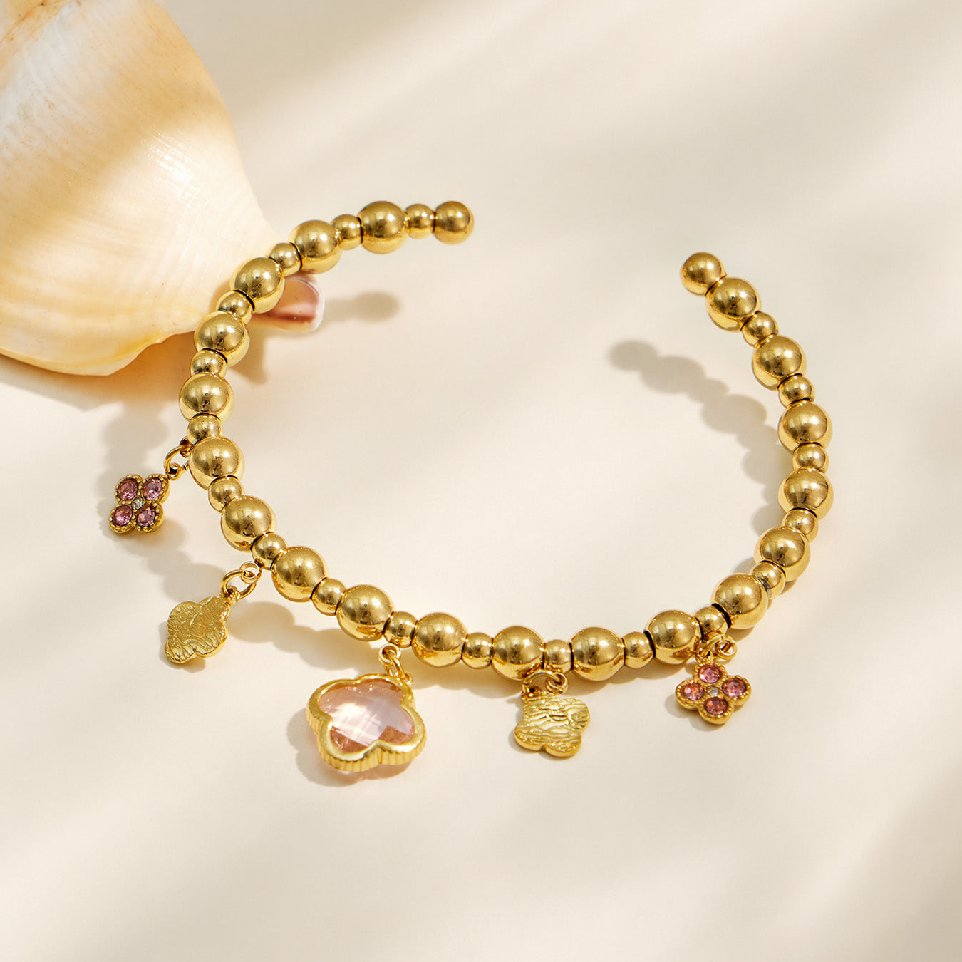 Pink four-leaf clover charm bracelet with a gold beaded chain displayed on fabric