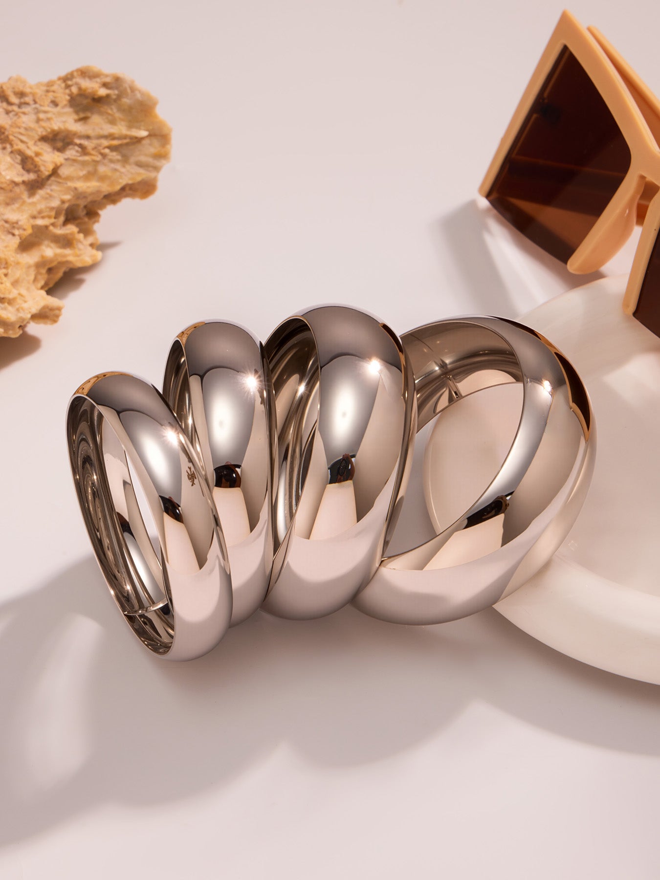 polished silver stainless steel wide cuff bracelets displayed with natural stone and sunglasses, modern minimalist scene