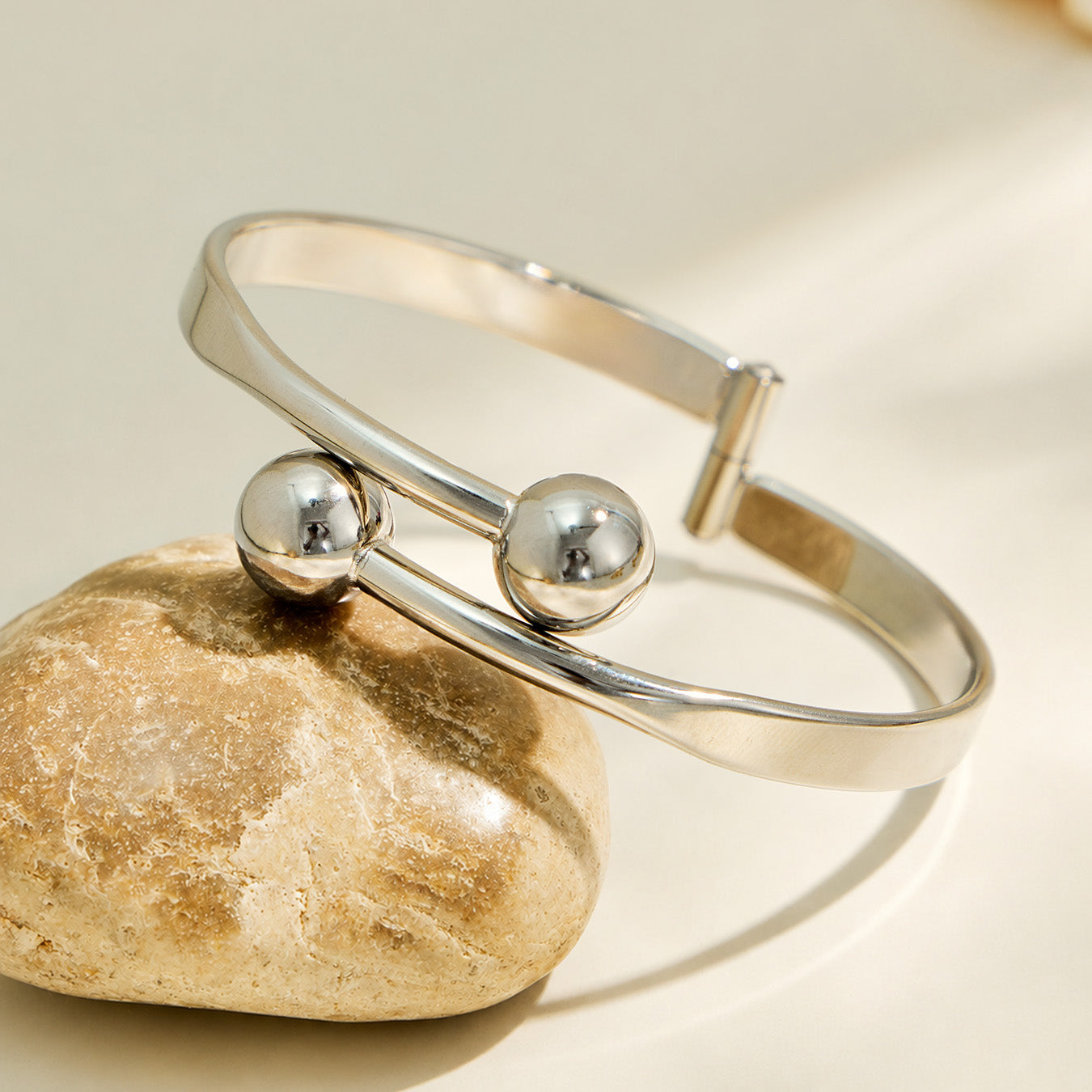 Polished steel double ball cuff bracelet displayed on a neutral stone prop