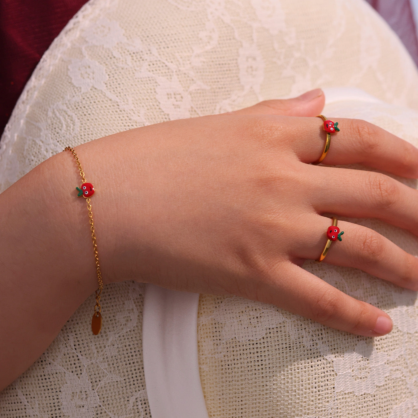 Red apple bracelet worn on a girl's wrist with delicate gold-tone chain and colorful apple charm