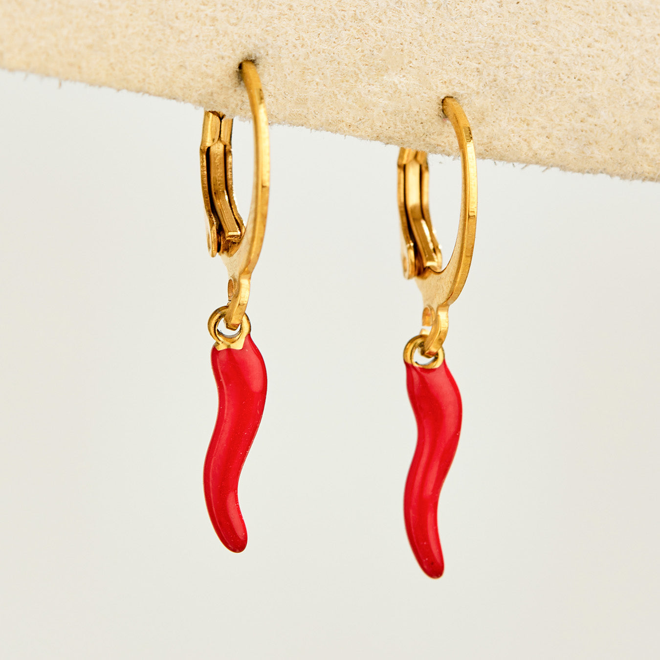 Pair of gold huggie earrings with bright red chili pepper charms displayed on a light background
