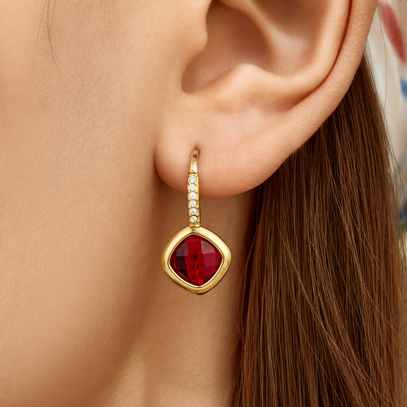 Side view of red glass stone drop earrings worn on the ear
