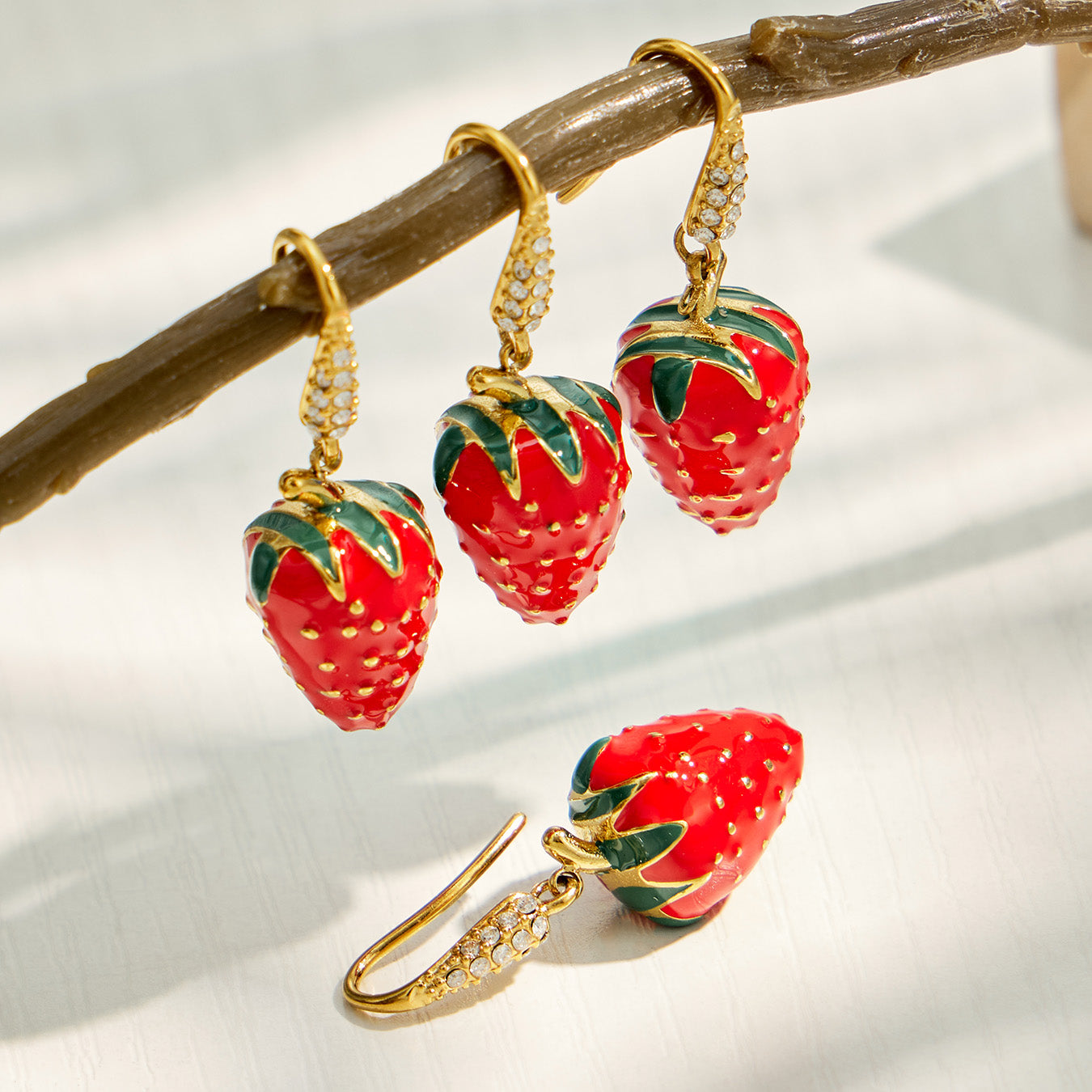Red strawberry earrings displayed in a lifestyle jewelry setting