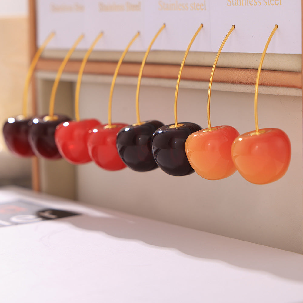 Resin cherry drop earrings arranged by color on a horizontal display stand