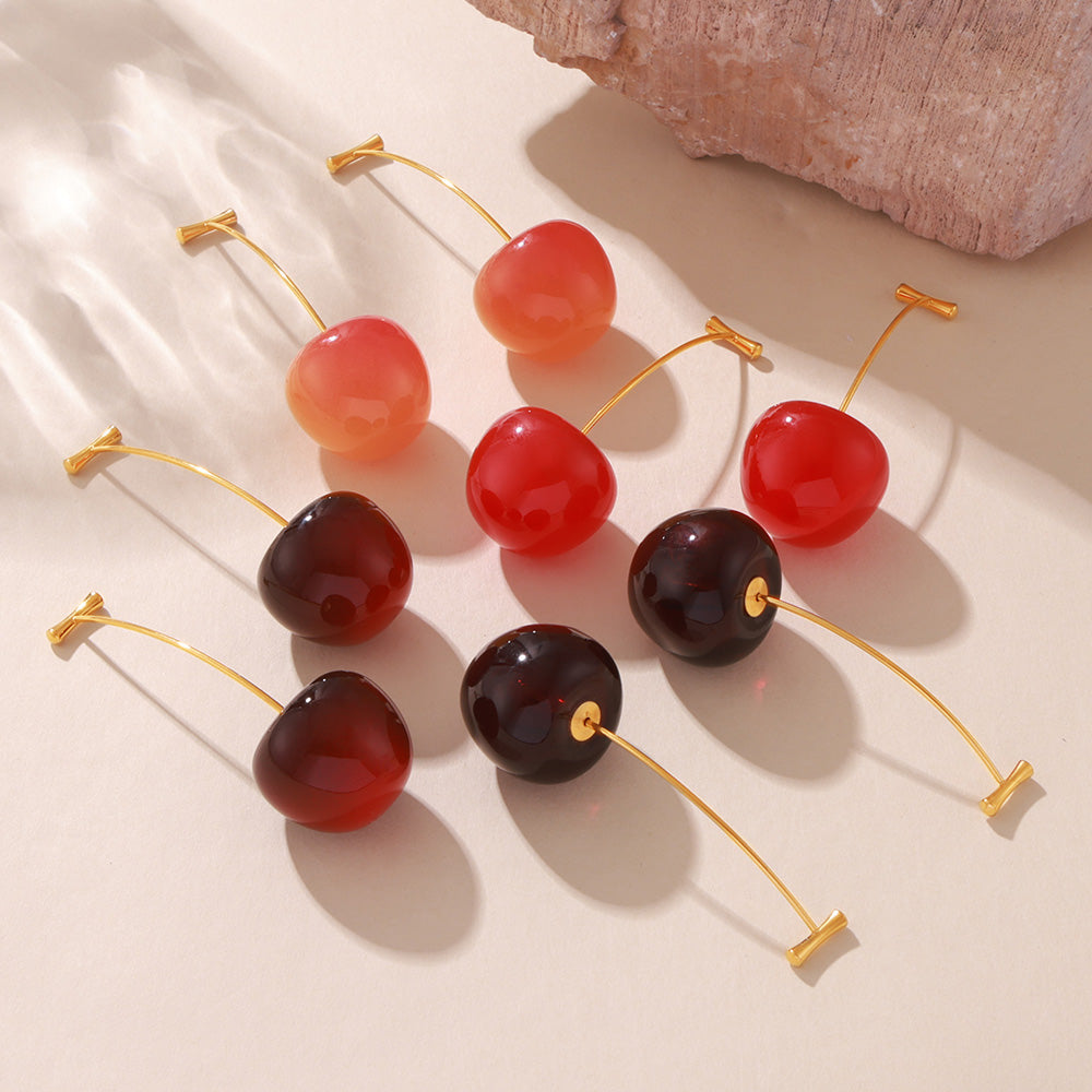 Four resin cherry earring color options arranged on a light satin background