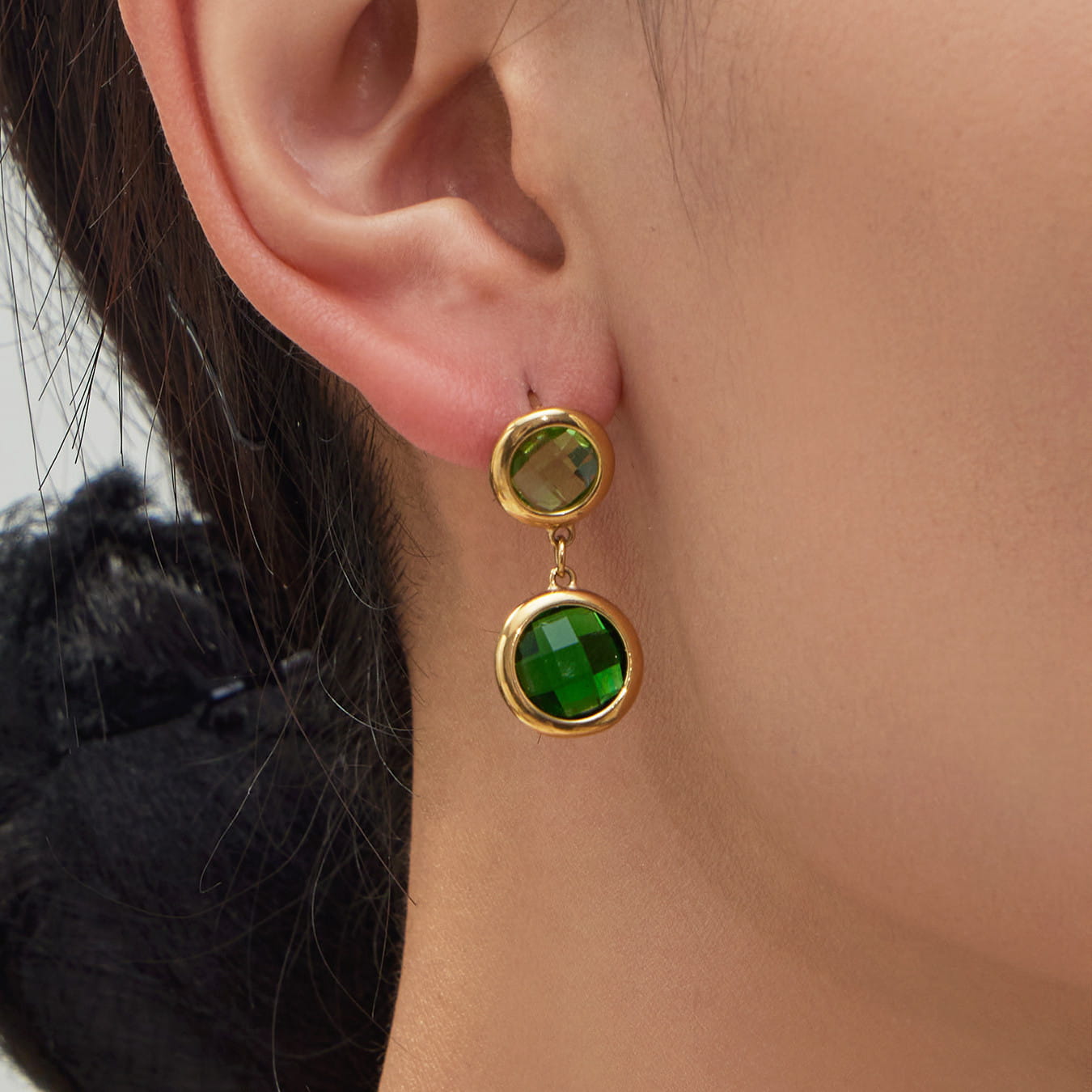 Close-up view of a model wearing a green glass stone drop earring made of nickel-free stainless steel.