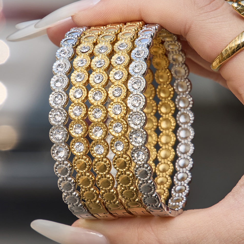 Hand holding gold H buckle zircon bangle bracelet with clear zircon accents and polished 18K PVD gold tone finish