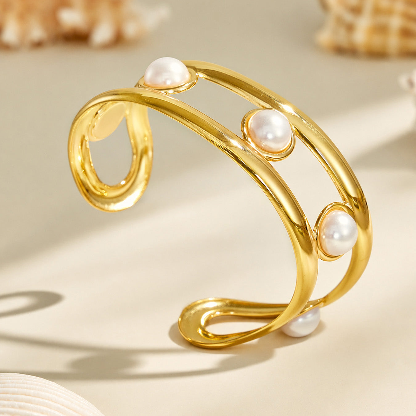 Sculptural gold cuff bracelet with white faux pearls displayed on a neutral surface