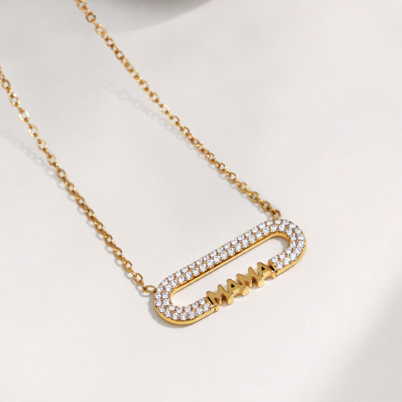 Single gold MAMA zircon bar necklace displayed on softly draped fabric