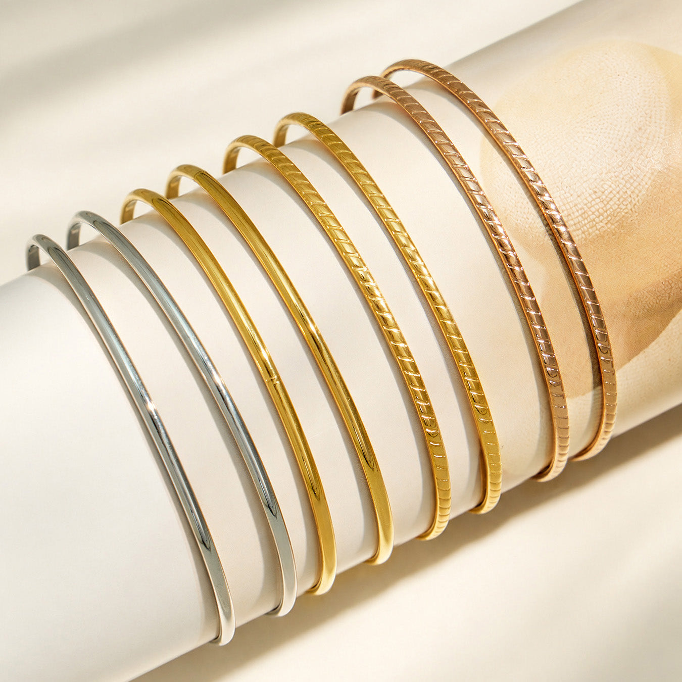 Slim stackable bangles in mixed steel, gold and rose gold finishes displayed on a cushion