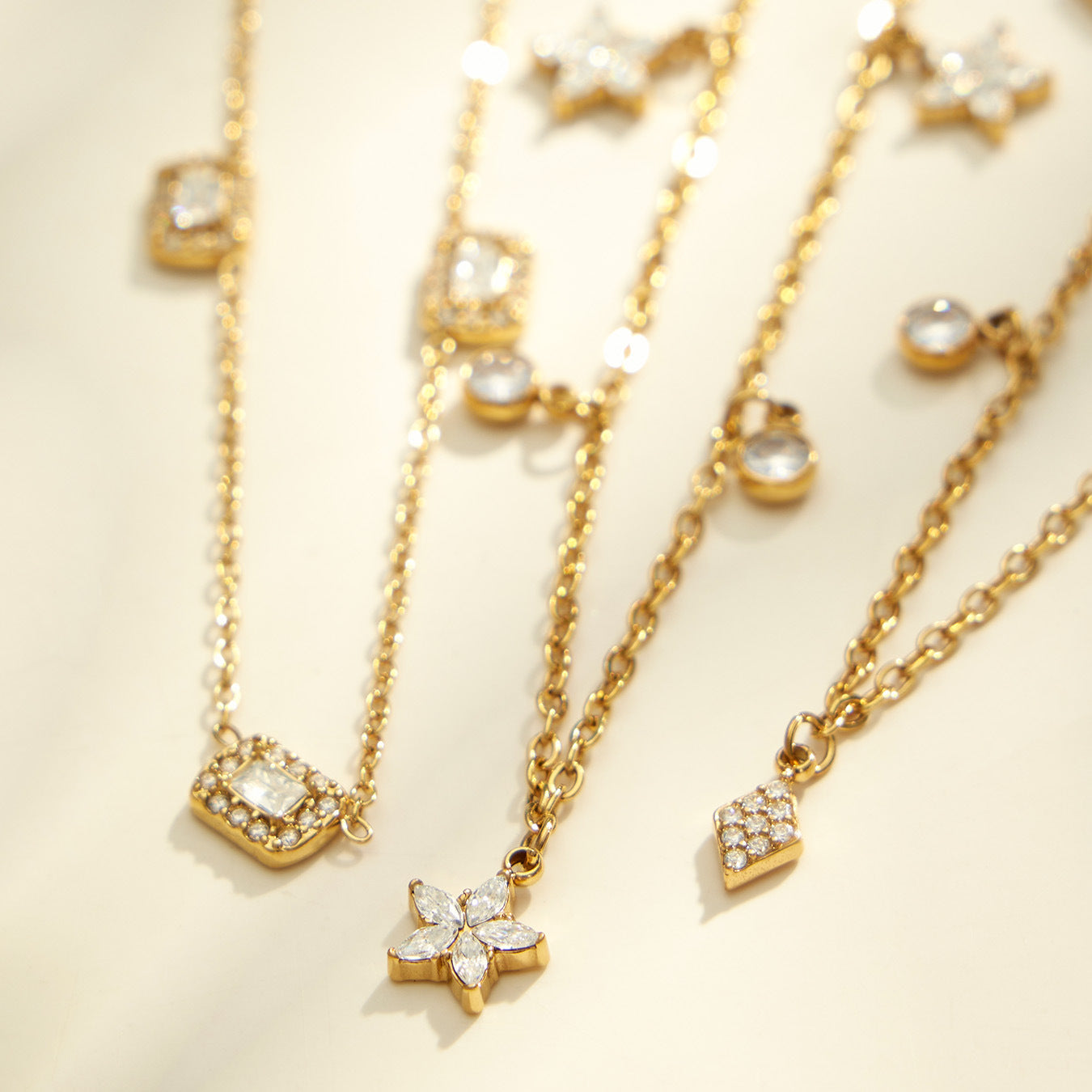 Close up of square and diamond zircon charm necklaces with polished 18K PVD gold chain details