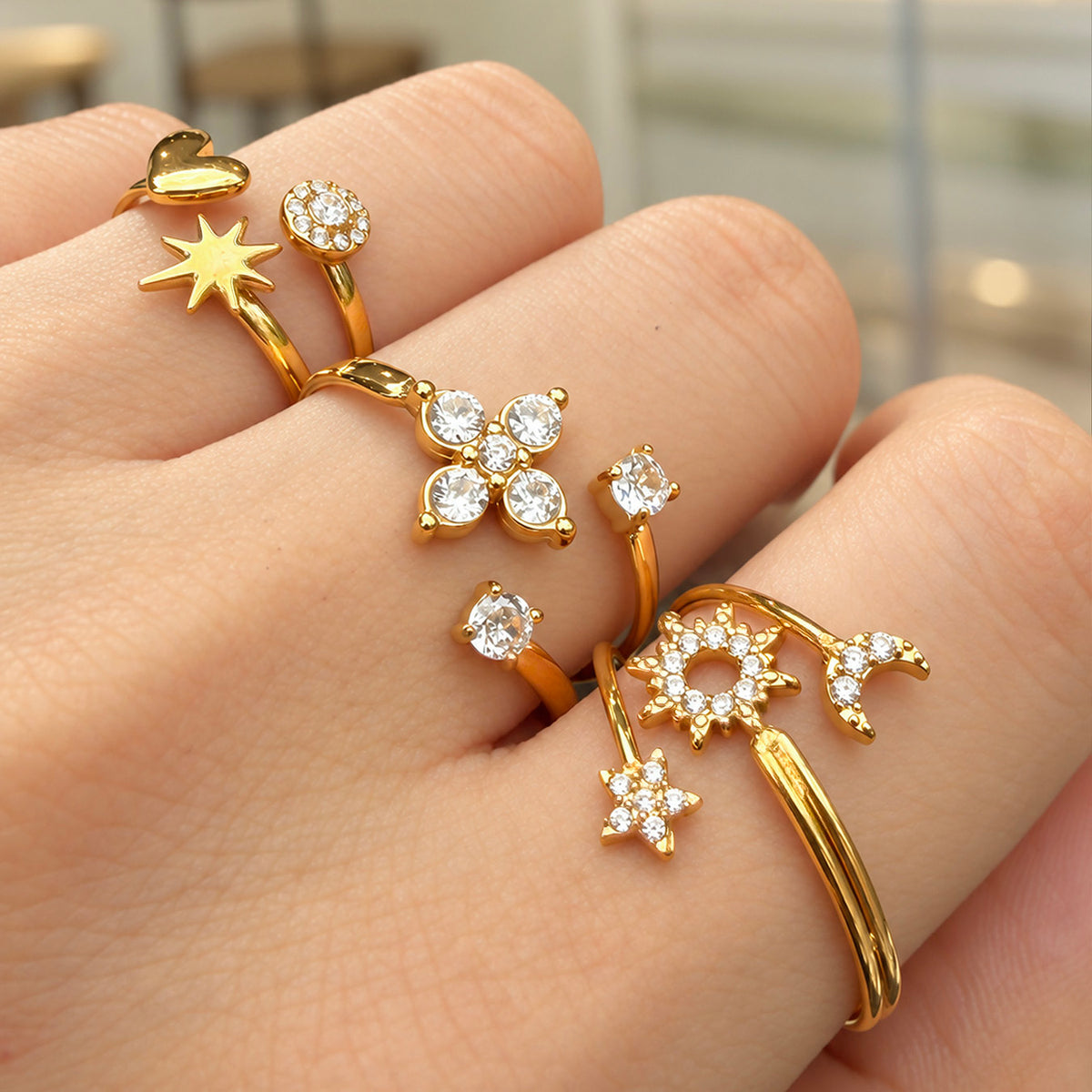 Front hand view of three gold-tone stainless steel open rings with clear stone accents
