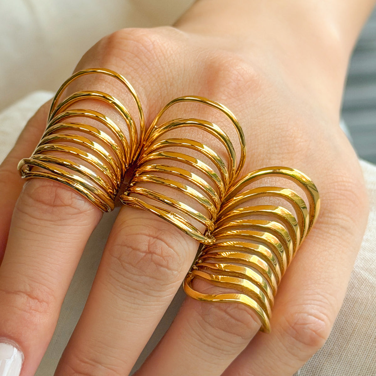 Three gold-tone stainless steel multi-band rings worn on adjacent fingers, showing their curved layered designs