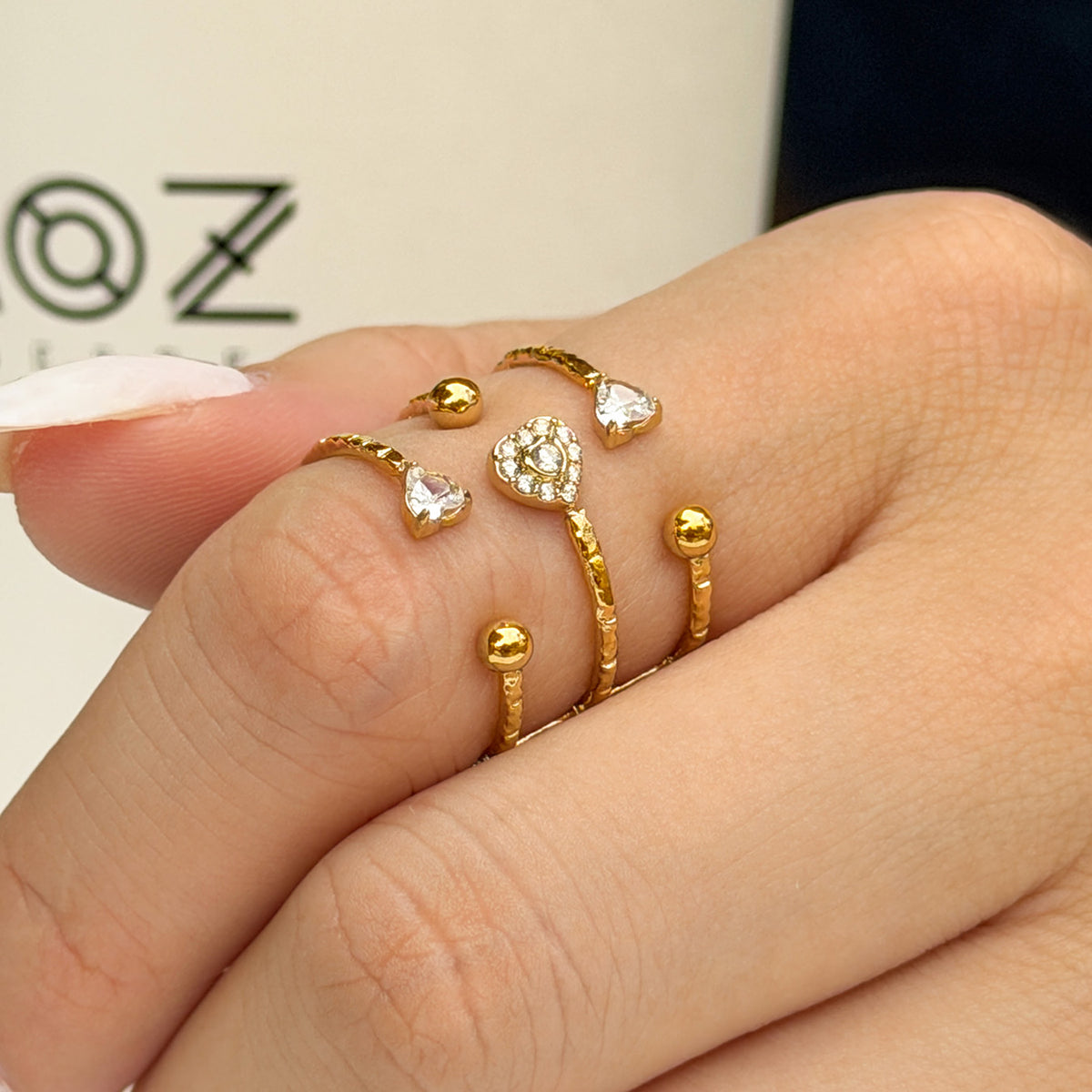 A403 gold-tone stainless steel heart and bead open ring worn on a finger beside a white cup