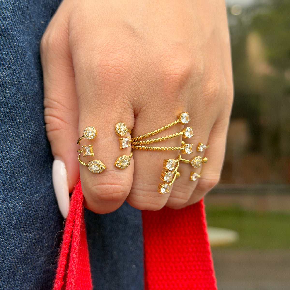Gold-tone heart, geometric and stone-tip rings worn on a hand holding a red bag strap