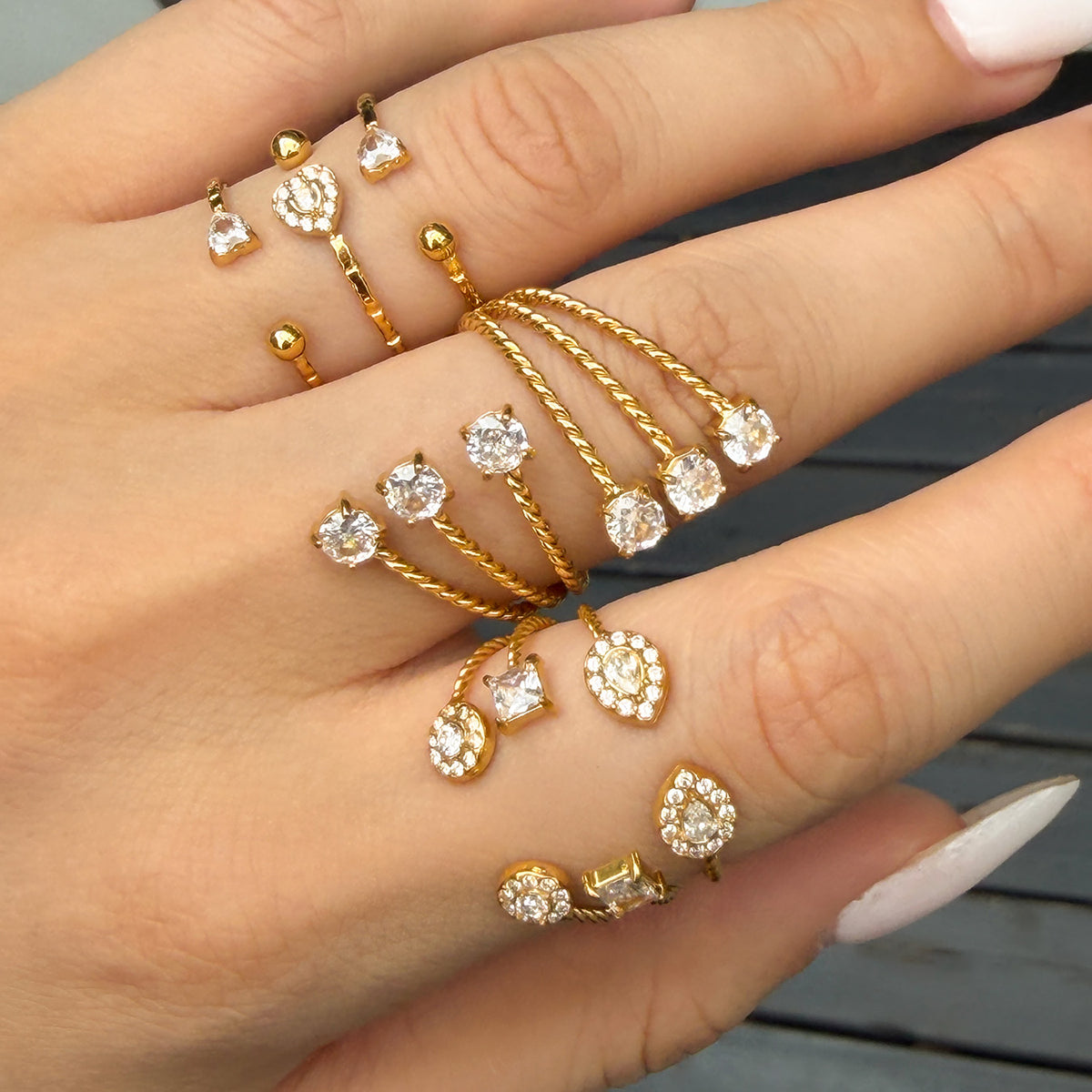 Angled side view of gold-tone open rings on fingers, showing layered bands and raised decorative details