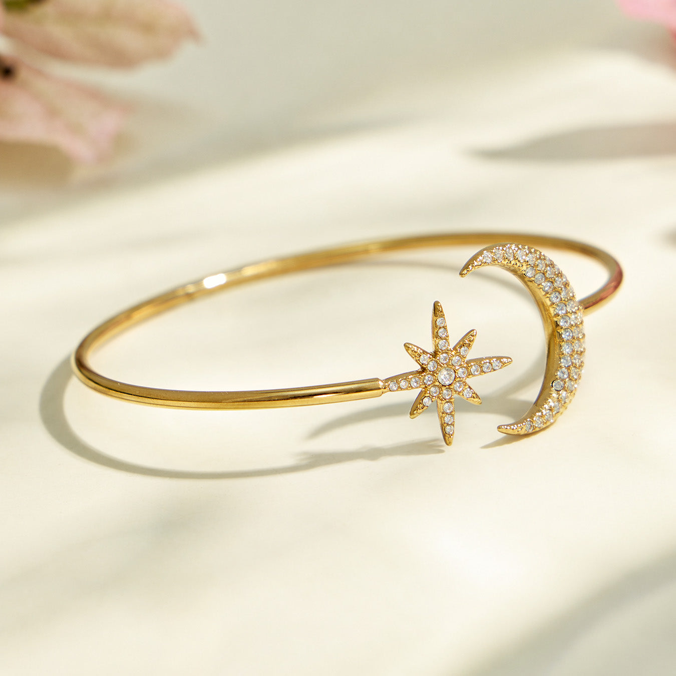 Gold star and moon open cuff bracelet displayed on a light neutral background