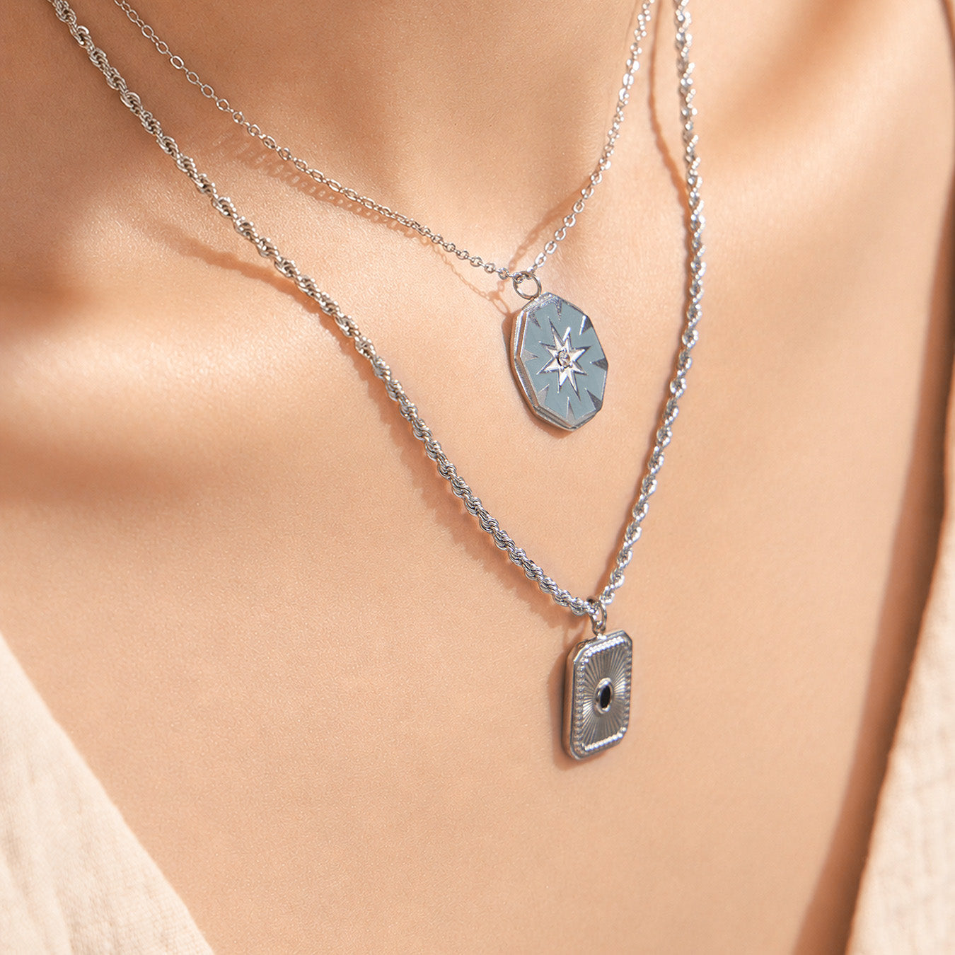 Model wearing layered starburst and square pendant necklaces in polished 316L stainless steel