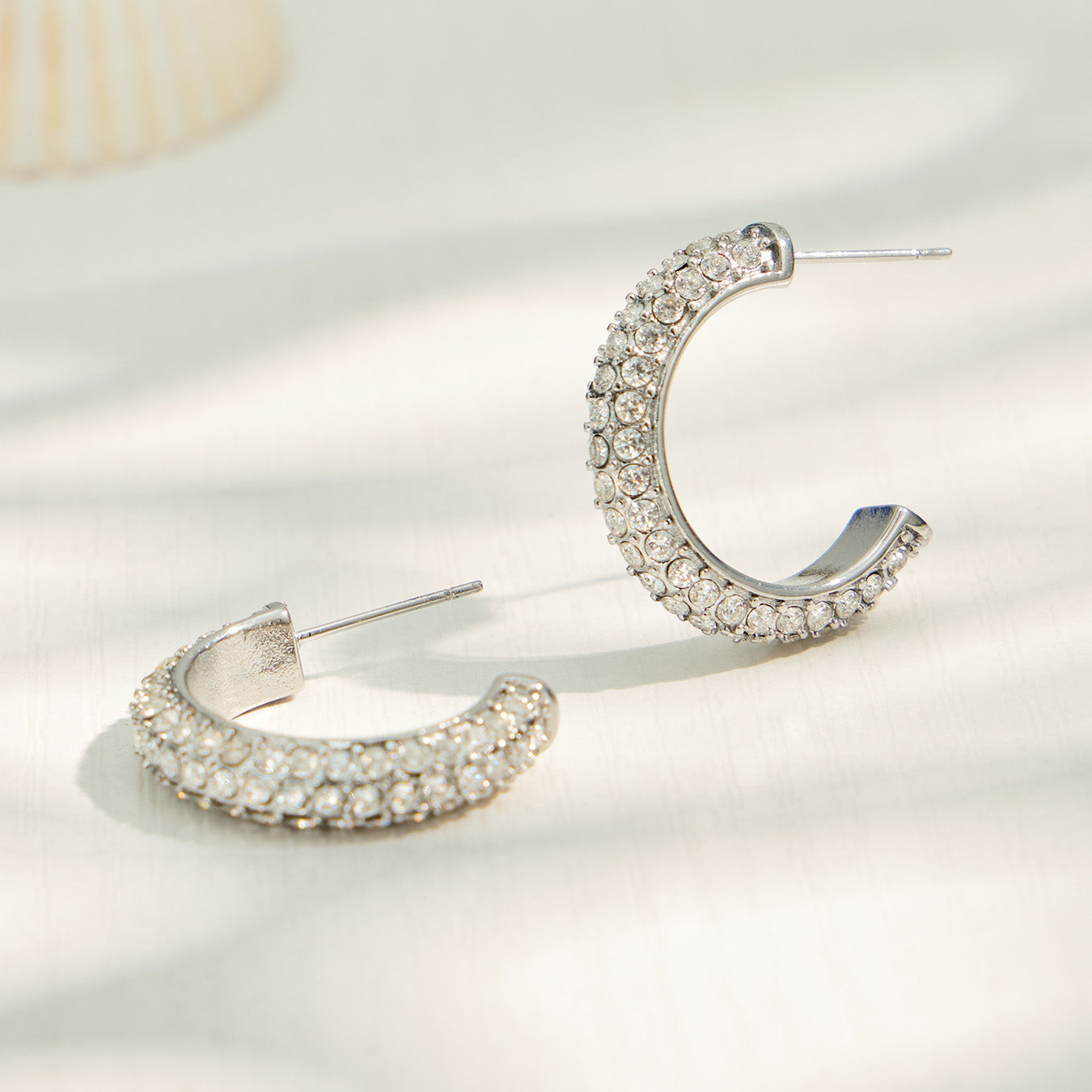 Steel-tone C-shaped cubic zirconia hoop earrings in a product display