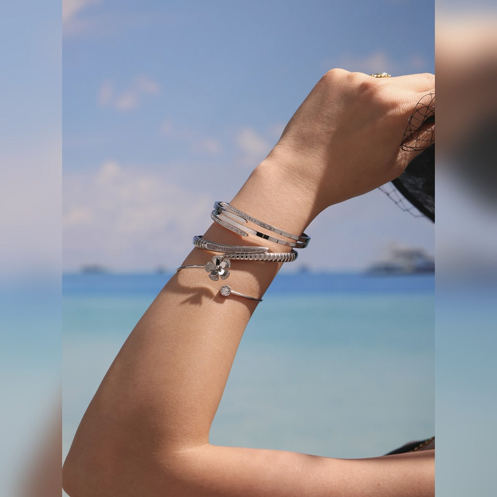 Close-up of a gold-tone nail bangle bracelet layered with slim bangles in a seaside setting