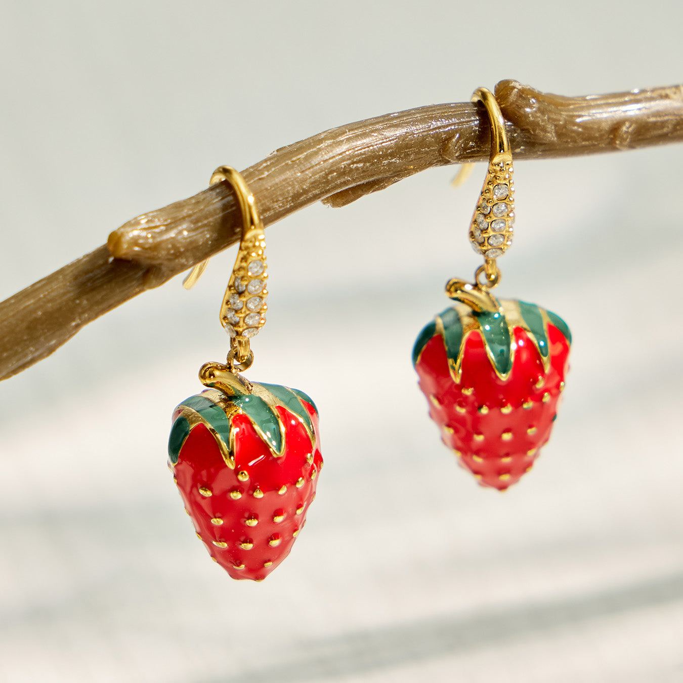 Strawberry drop earrings hanging in a gold-tone jewelry display