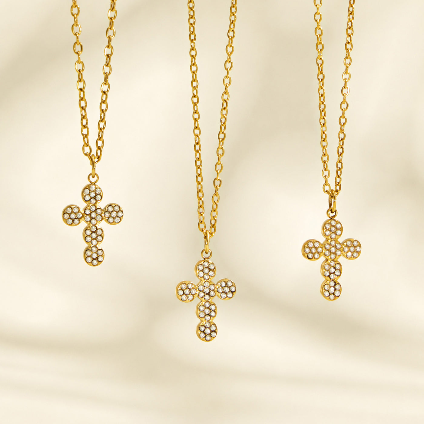 Three gold cross pendant necklace designs displayed vertically on a cream background