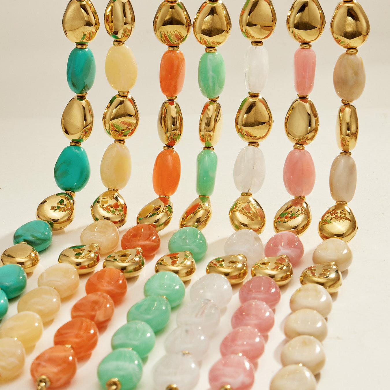 Colorful oval resin bead jewelry strands with polished gold-tone accents arranged in a vertical display