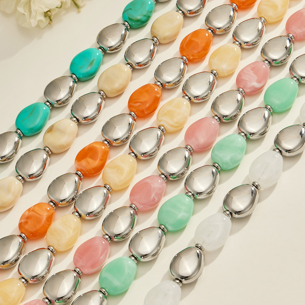 Close-up of colorful oval resin bead strands with polished steel-tone accents arranged in parallel rows