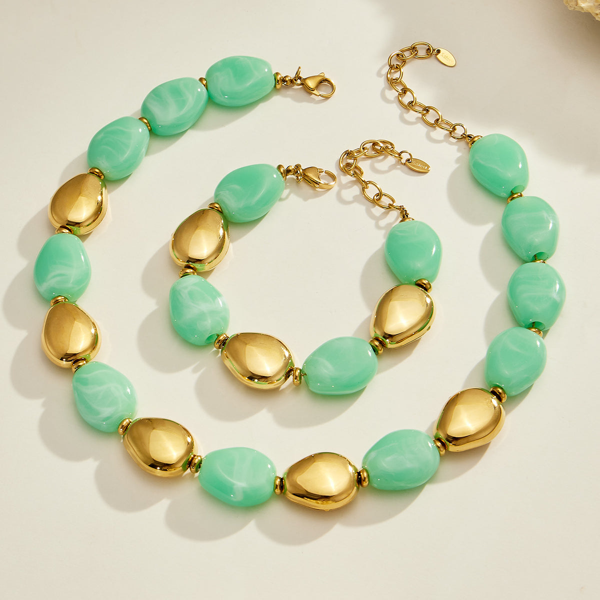 Light green oval resin bead necklace and matching bracelet with polished gold-tone accents displayed together