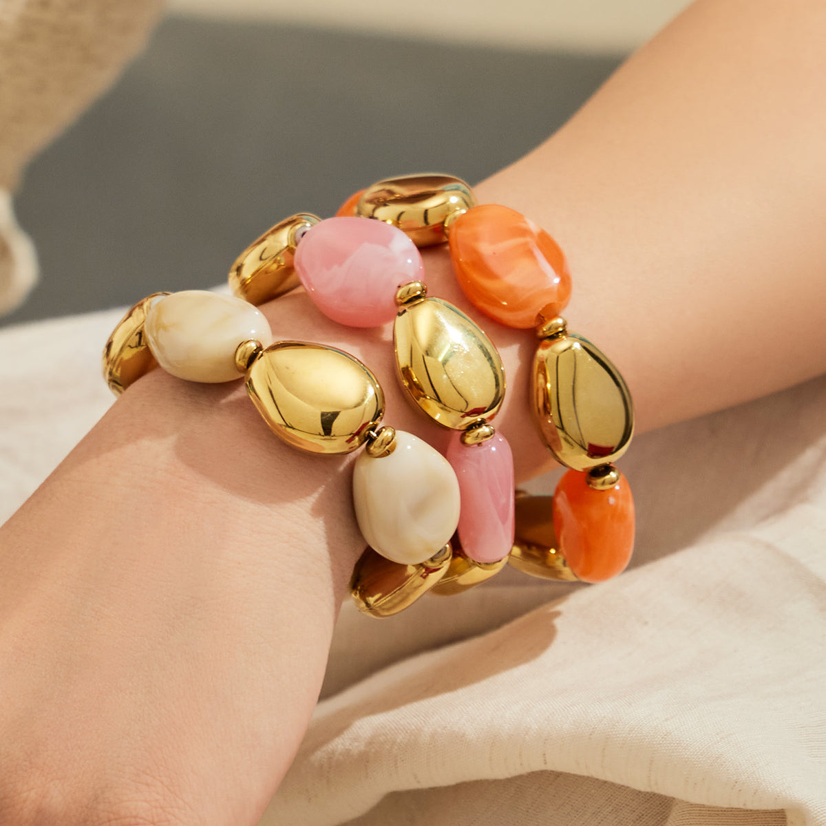 Model wearing stacked ivory pink and orange-toned resin bead bracelets with polished gold-tone accents