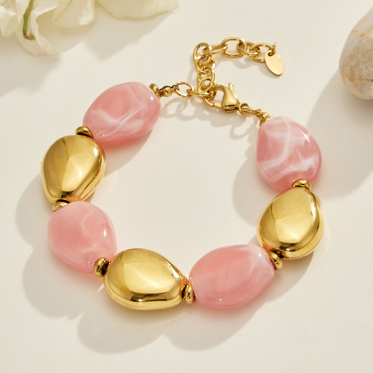Pink oval resin bead bracelet with polished gold-tone accents and an adjustable extension chain displayed flat