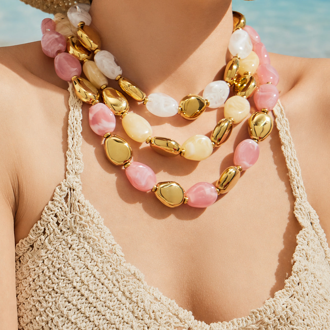 Close-up of layered pink white and ivory oval resin bead necklaces with polished gold-tone accents on a model
