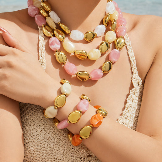 Model wearing layered pink white and ivory resin bead necklaces with coordinating stacked bracelets and gold-tone accents