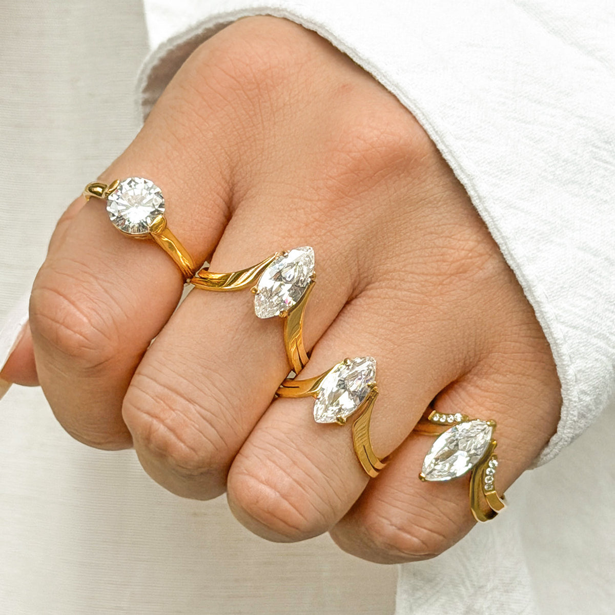 Gold zircon rings with round and marquise center stones displayed on curled fingers beside a white sleeve.