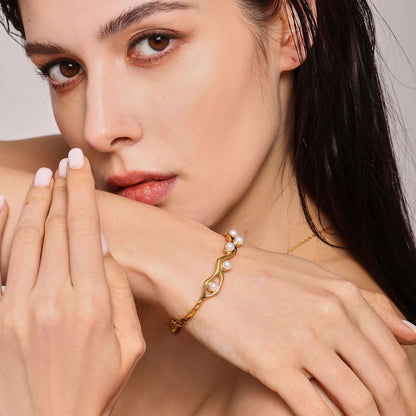 Woman wearing 18K gold plated titanium steel C-shaped open bangle with faux pearls and branch texture