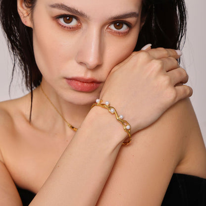 Woman wearing 18K gold plated titanium steel C-shaped open bangle with faux pearls and branch texture