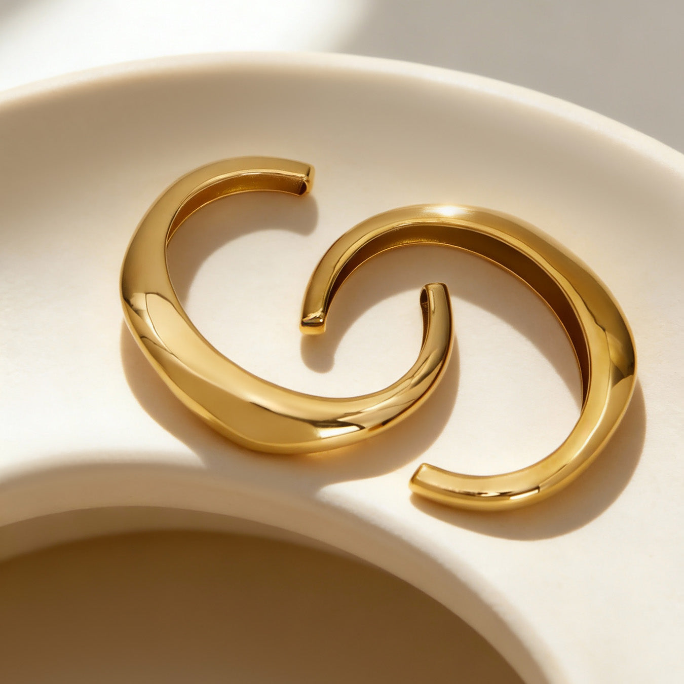 18k gold c-shaped polished stainless steel bracelets displayed in bowl, sleek fashion accessory