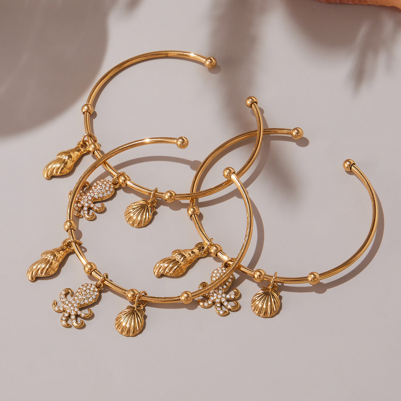 18K gold ocean shell/octopus bangle set displayed on beige background, luxury beach jewelry