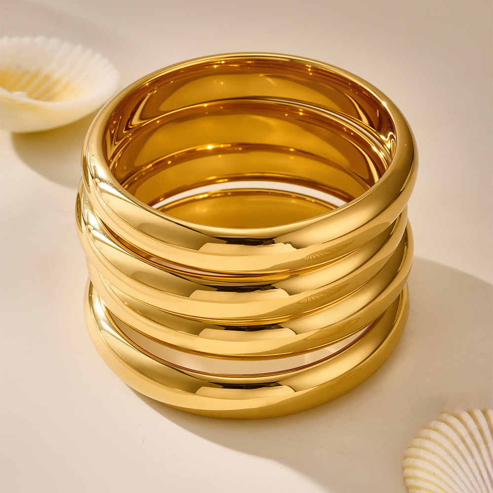 Stacked 18K gold plated luxury bangles displayed with seashells, high-end jewelry