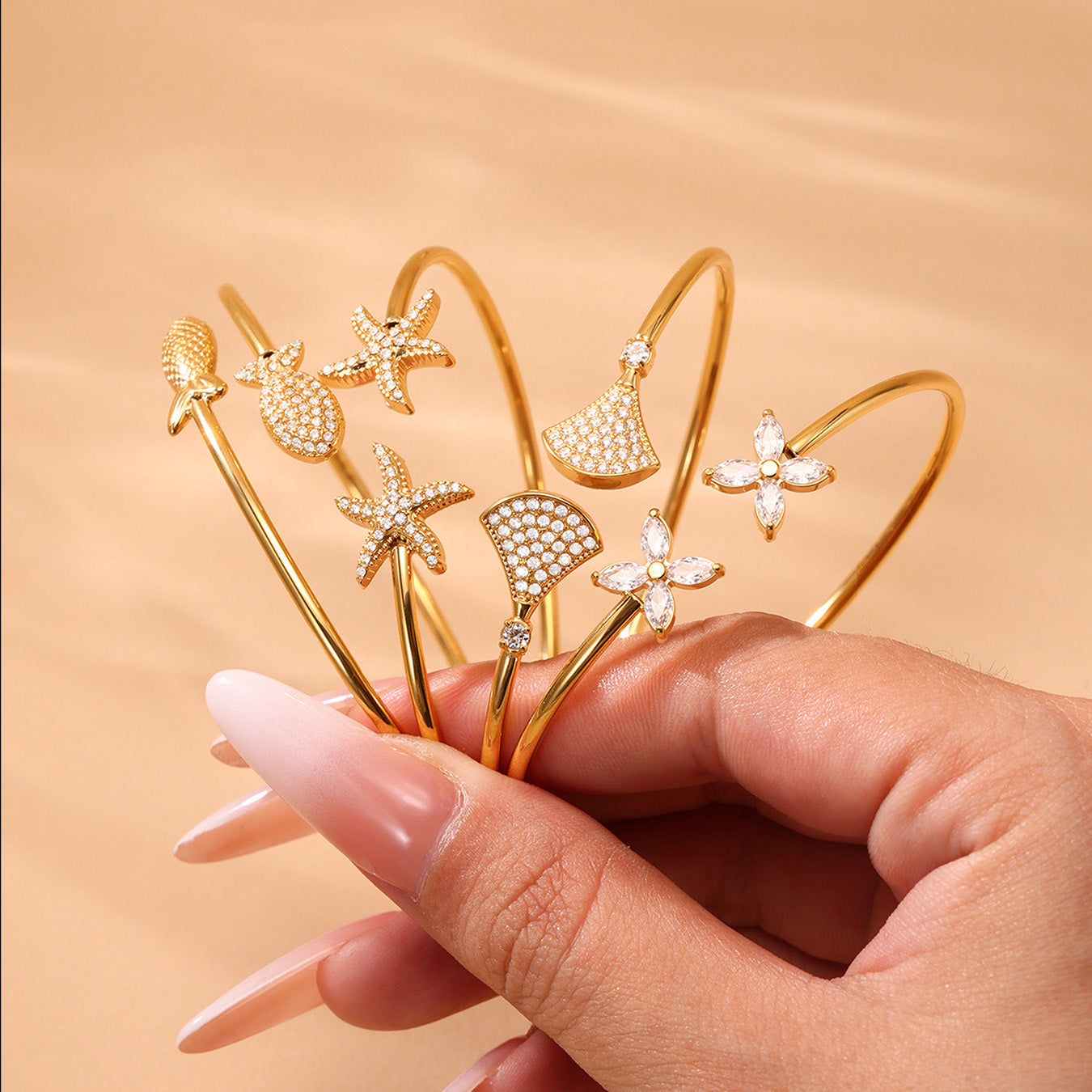Hand holding 18k gold plated ocean 5A zircon bangle set: fish starfish design with 5A zircon