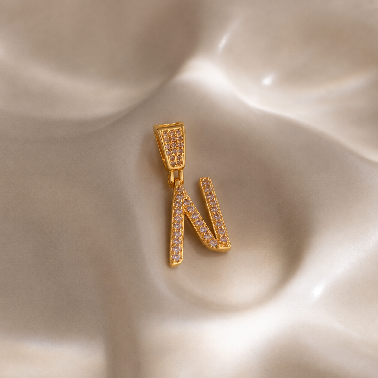 Close-up of 18K gold plated zircon N initial pendant charm with pavé stones on satin background