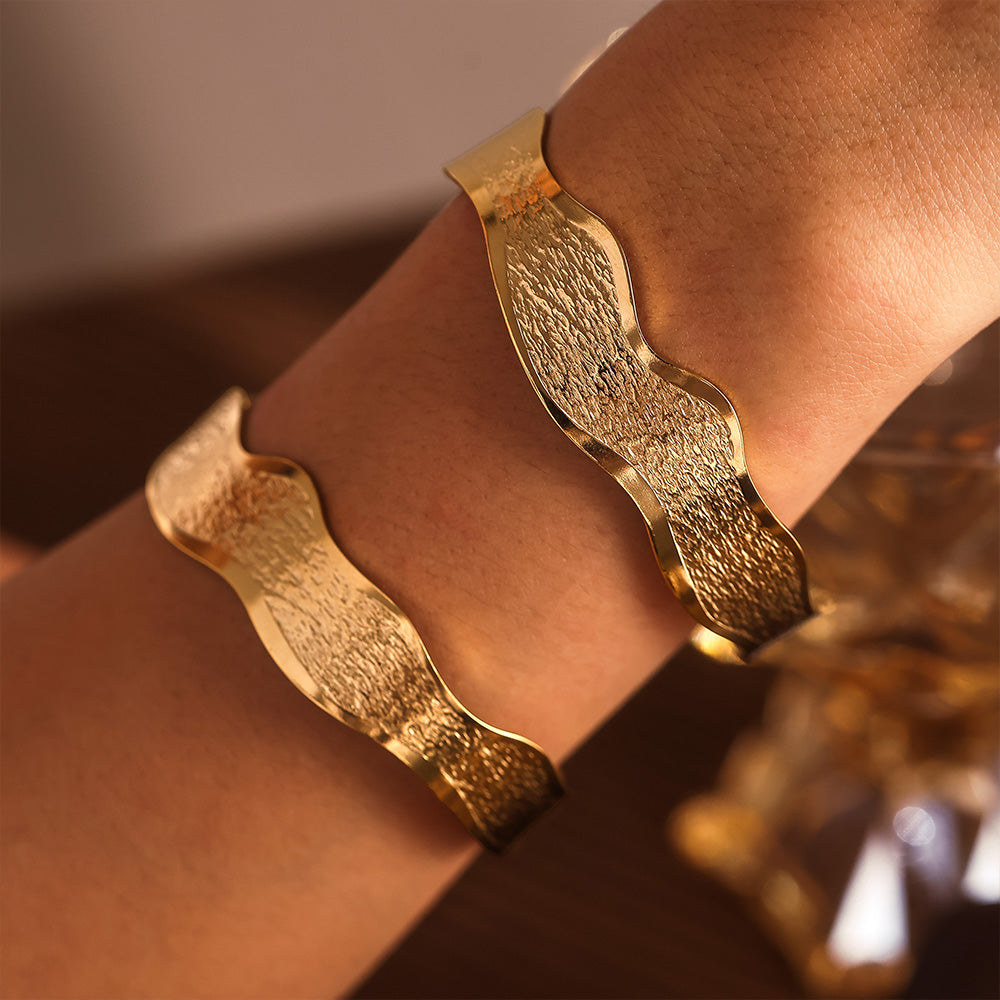 Stacked 18K gold wave texture open bangles on wrist, trendy layered style