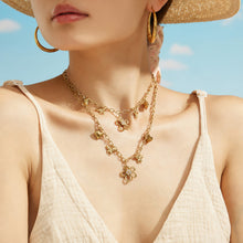 18K PVD gold butterfly and flower charm necklace styled on a model by the beach