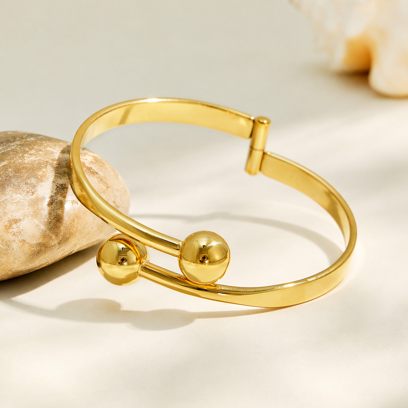 18K PVD gold double ball cuff bracelet displayed in a soft neutral flat lay
