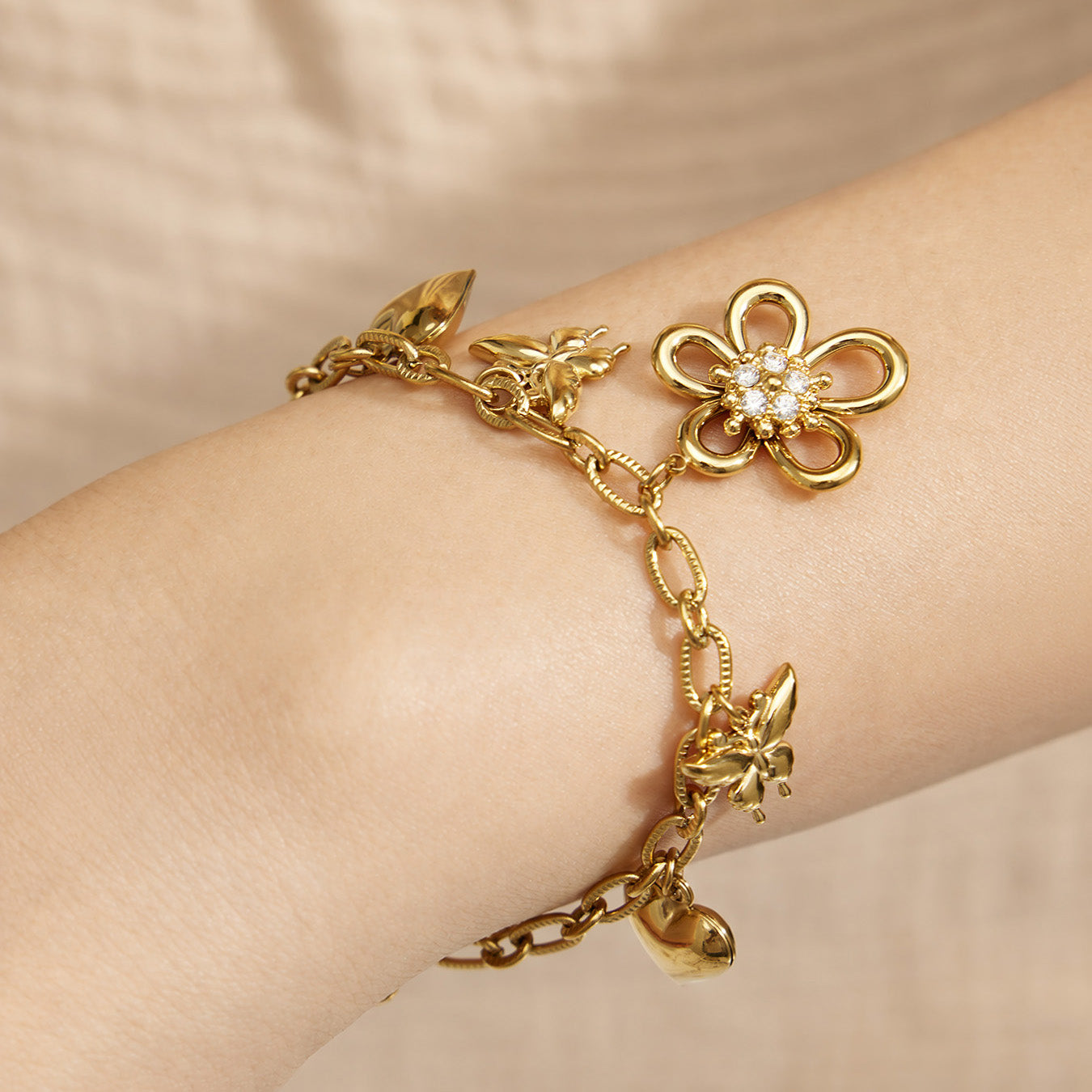 Close-up of an 18K PVD gold floral charm bracelet with butterfly and heart pendants