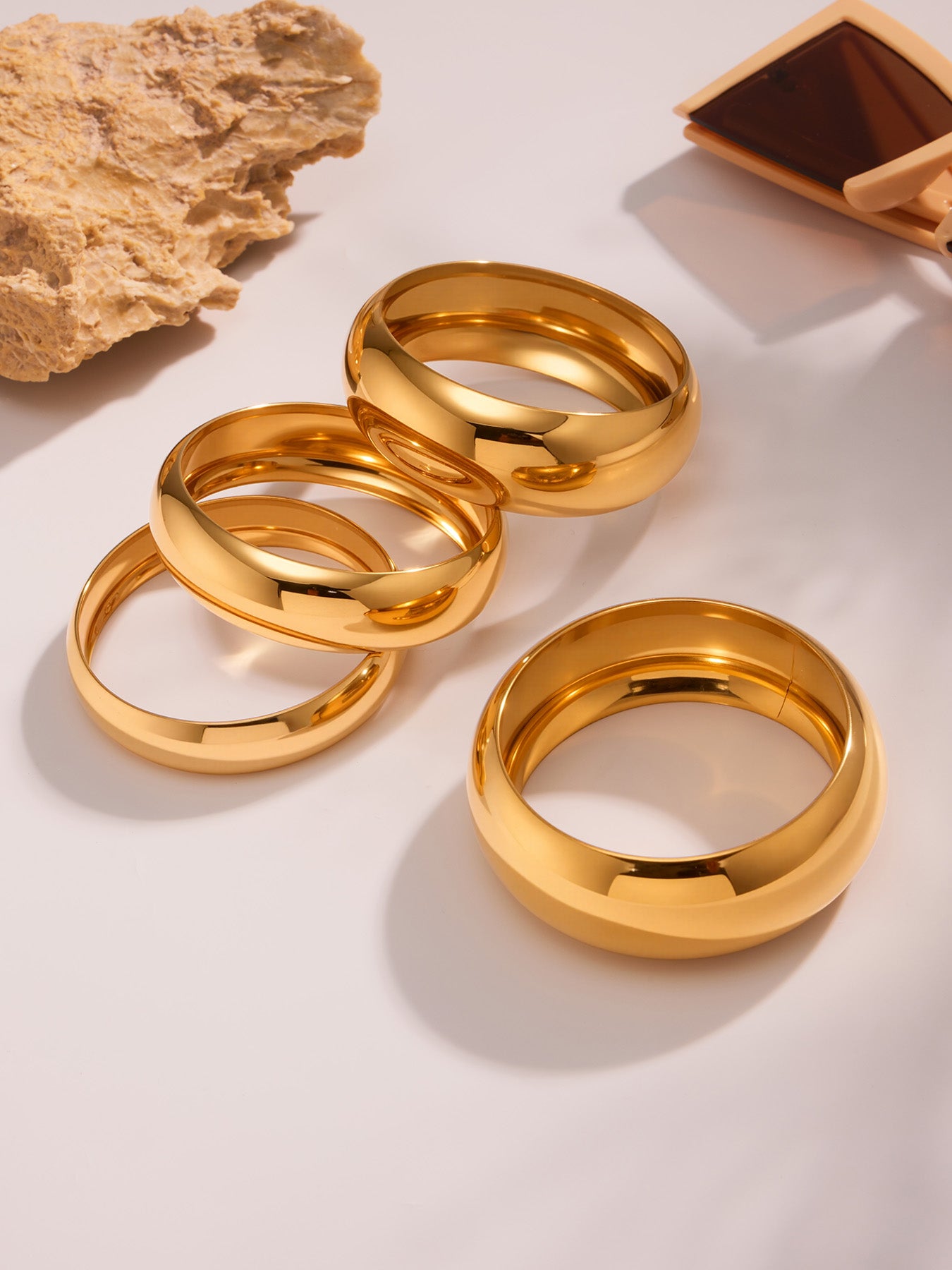 18k pvd gold plated stainless steel glossy wide cuff bracelets displayed with natural stone and sunglasses, stylish scene setup