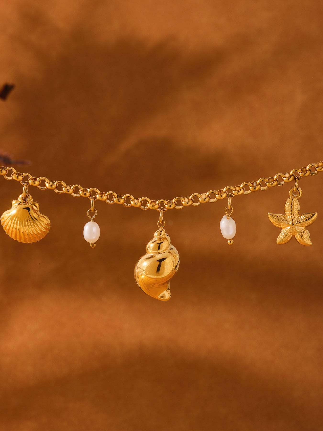 Detailed close-up of shell, conch, starfish and freshwater pearl charms on gold chain, coastal anklet bracelet wholesale design