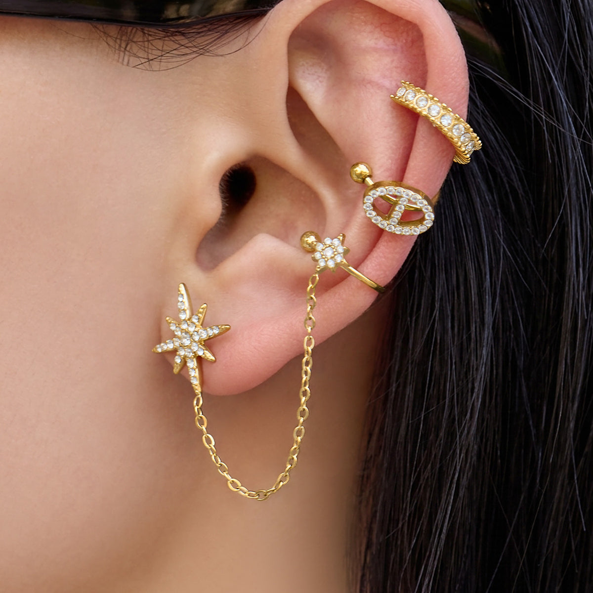 Close-up of an 18K PVD gold starburst chain ear cuff worn with small gold ear accessories
