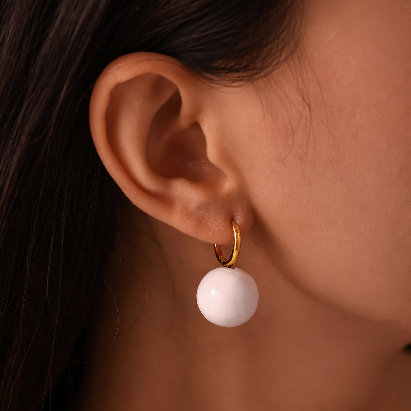 Side view of model wearing white ball drop earrings with gold-tone hoops