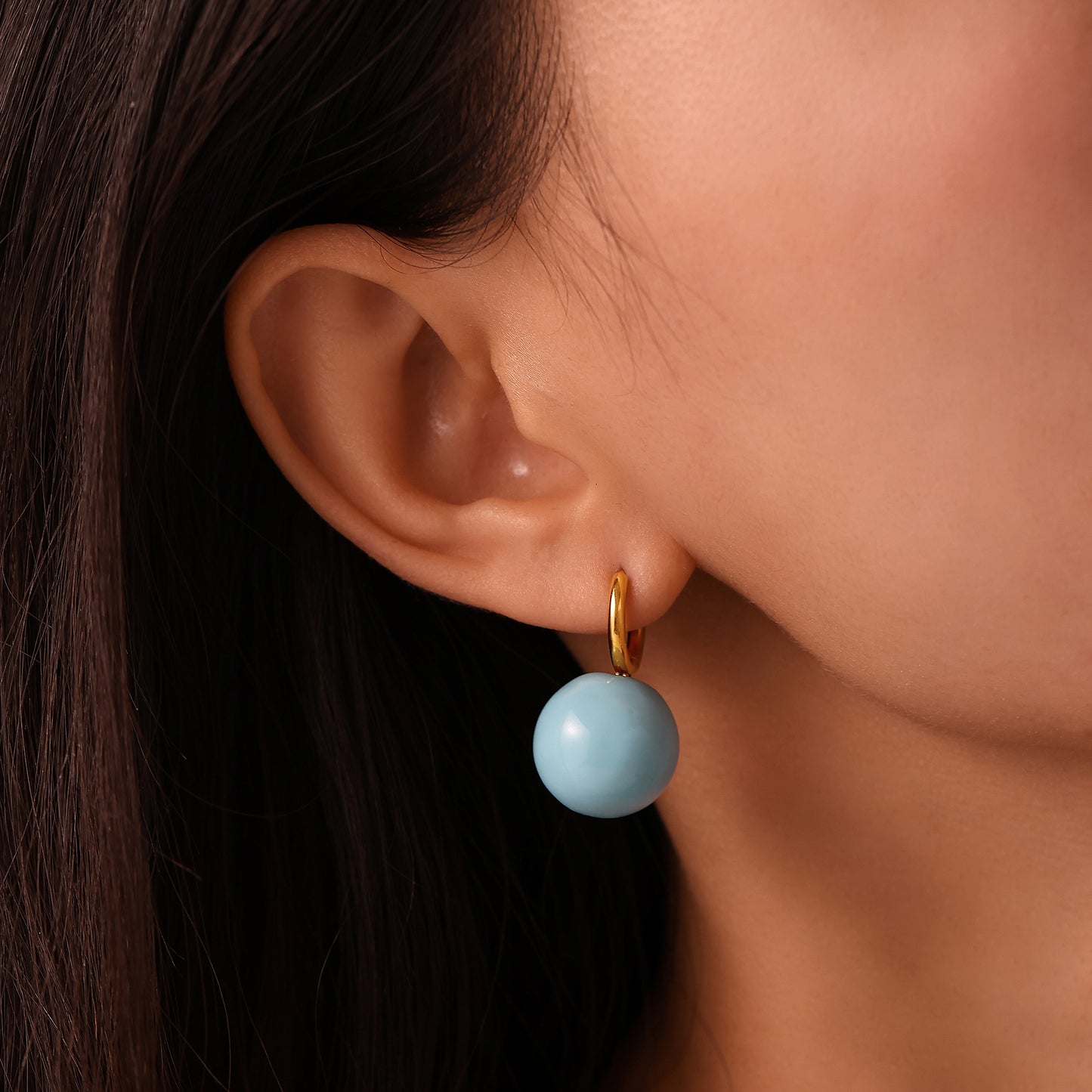 Side view of model wearing a light blue ball drop earring with a gold-tone hoop